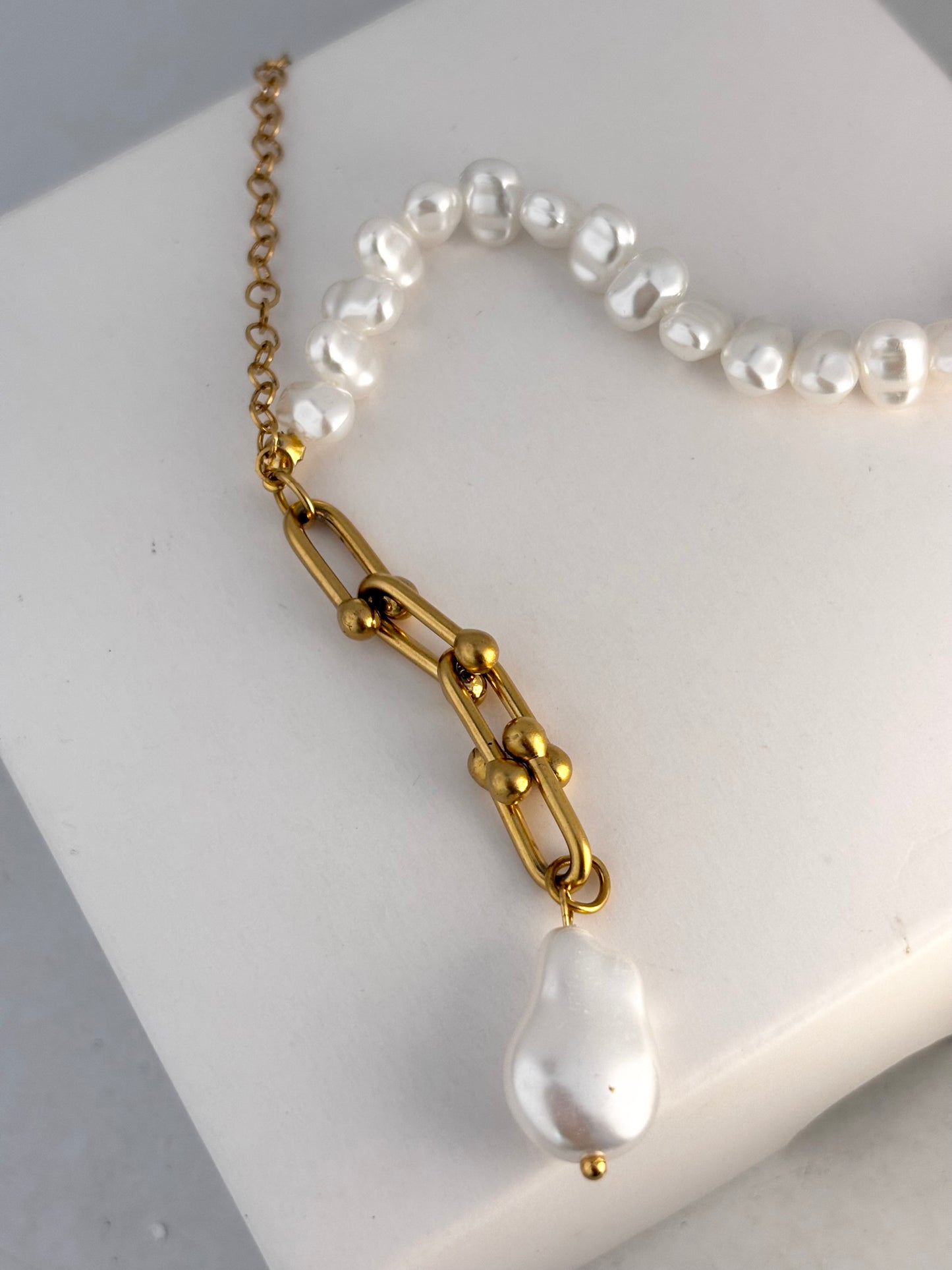 Pearl necklace with gold chain on a white surface