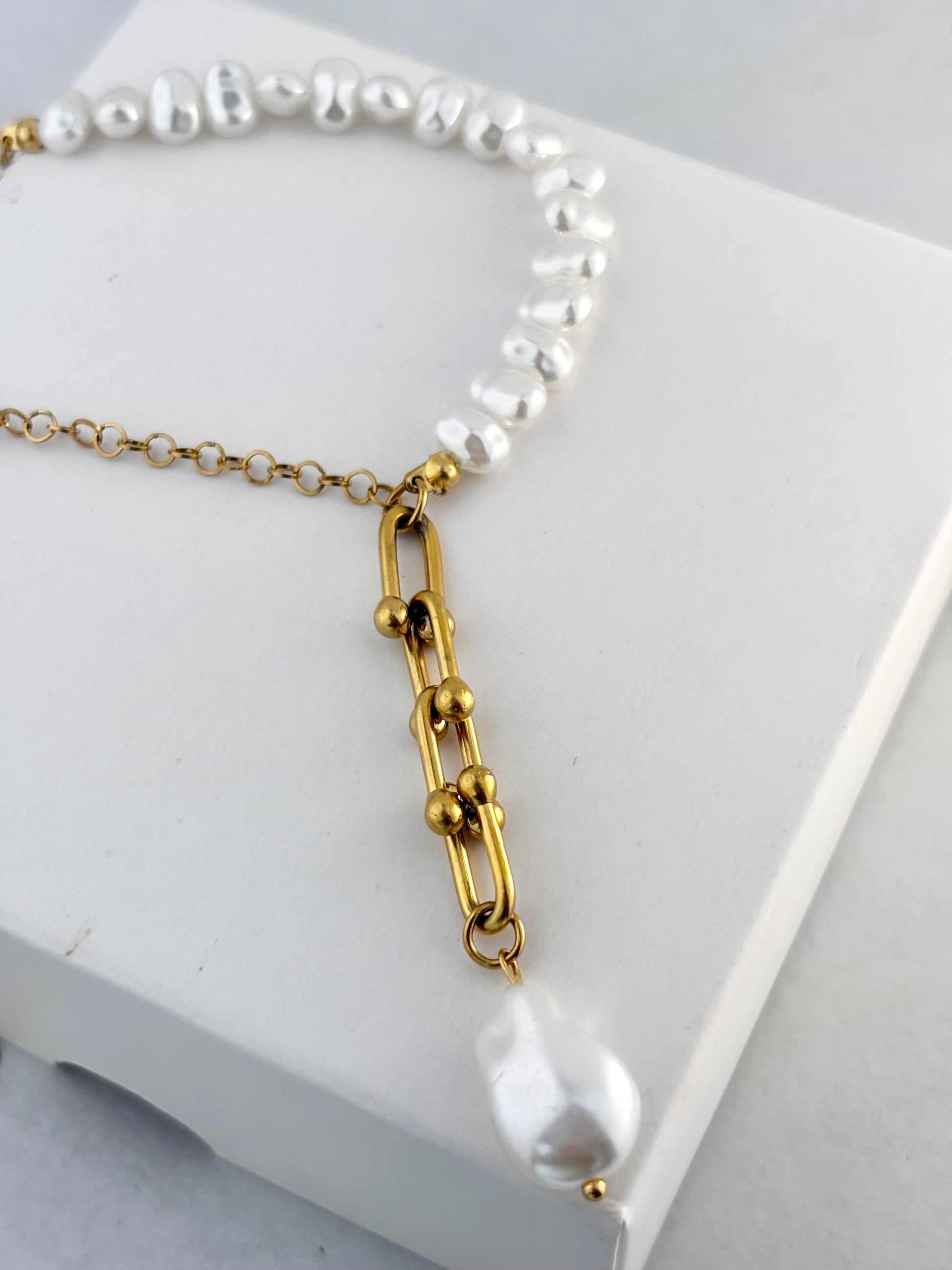 Pearl necklace with gold chain on a white surface