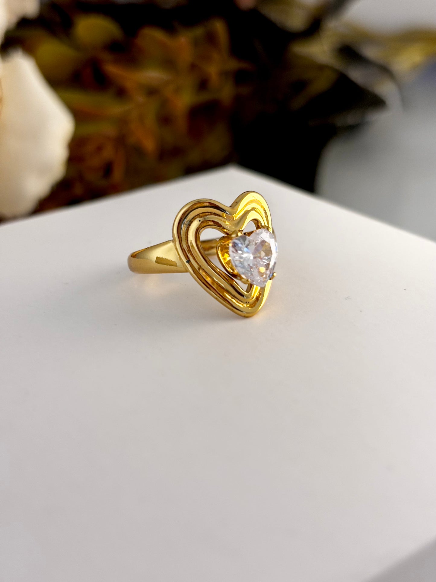 Gold heart-shaped ring with a clear gemstone on a white surface