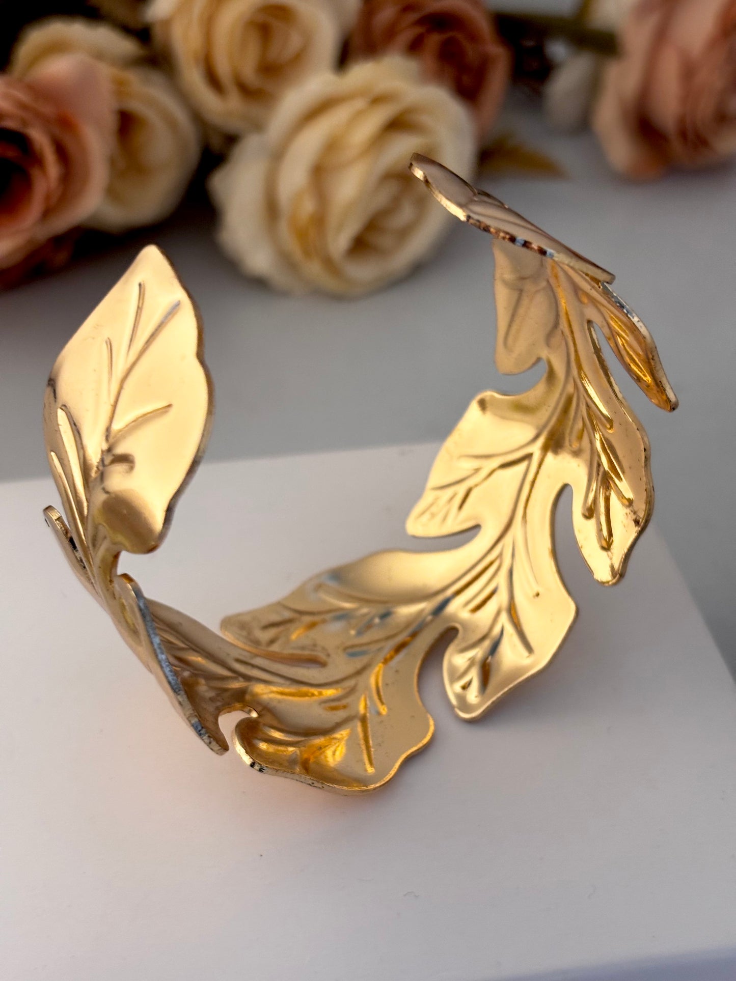 Gold leaf bracelet on a white surface with flowers in the background