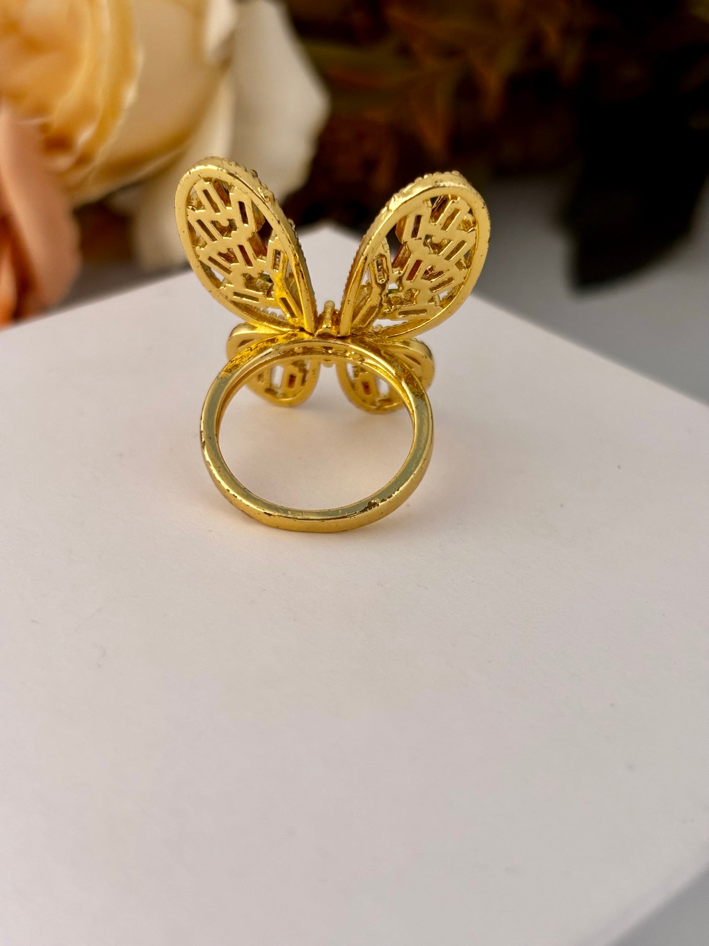 Gold butterfly-shaped ring on a white surface with blurred background