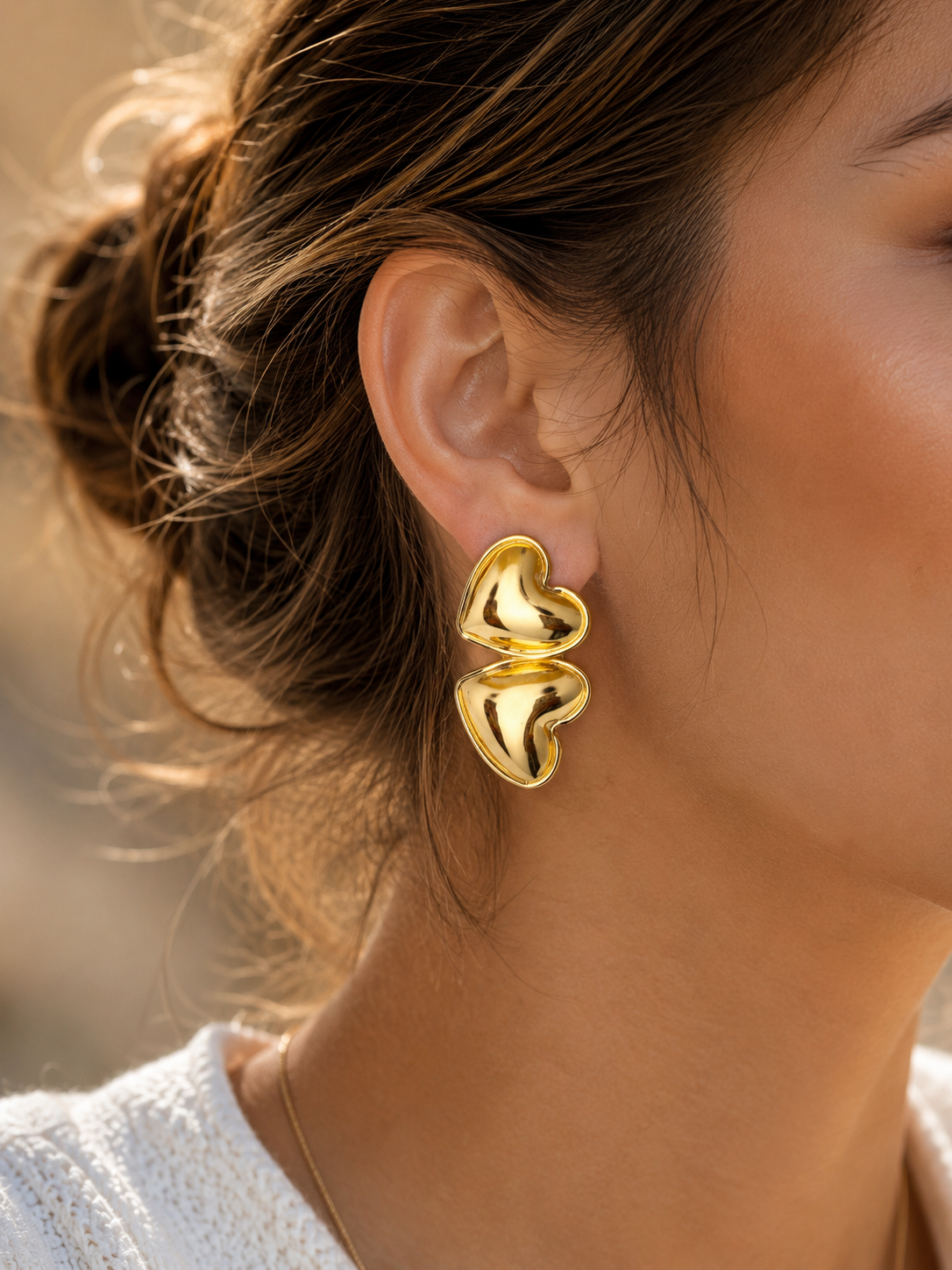 Close-up of a person wearing gold heart-shaped earrings with a blurred background.