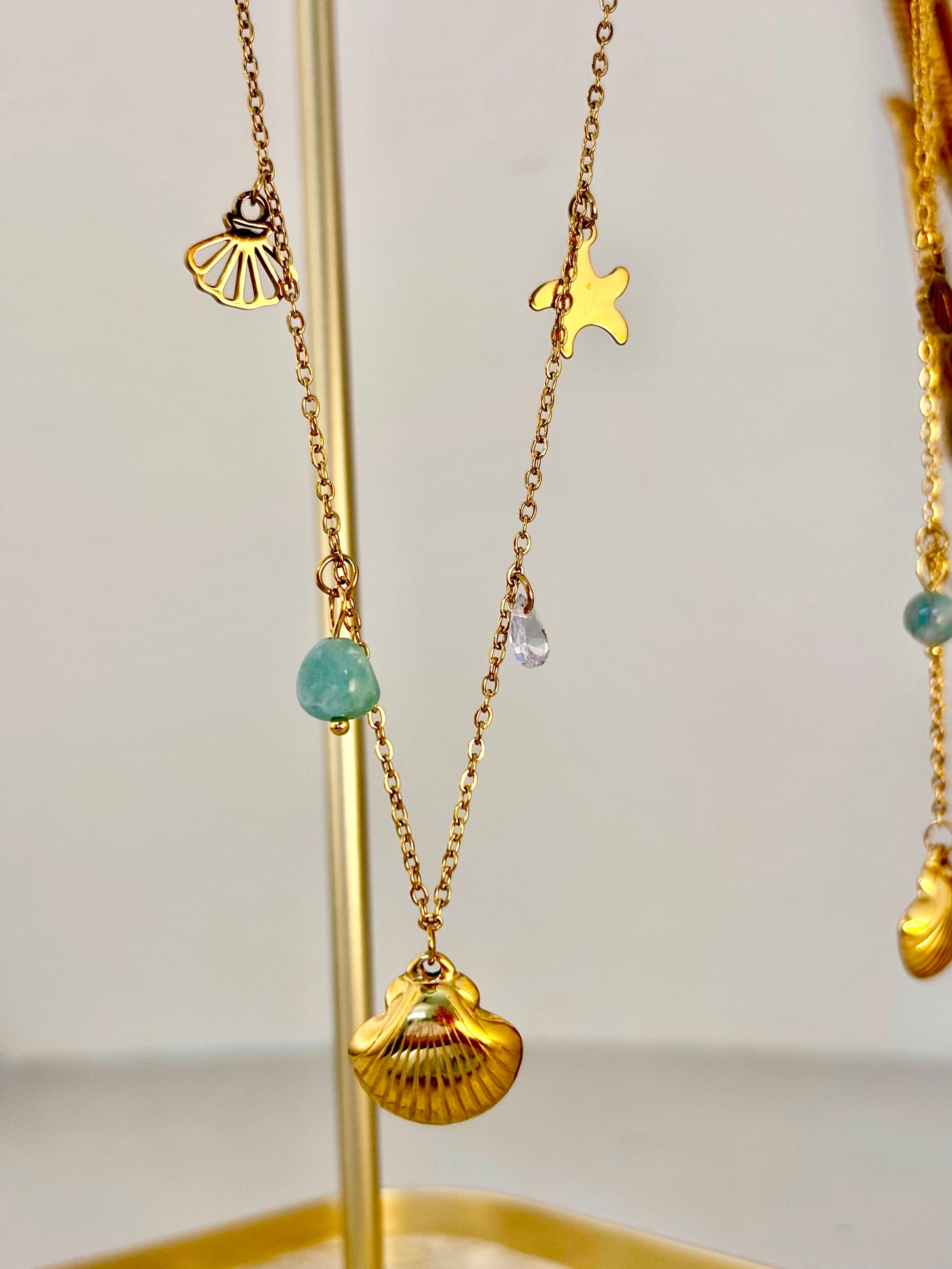 Gold necklaces with shell and star pendants on a stand against a light background