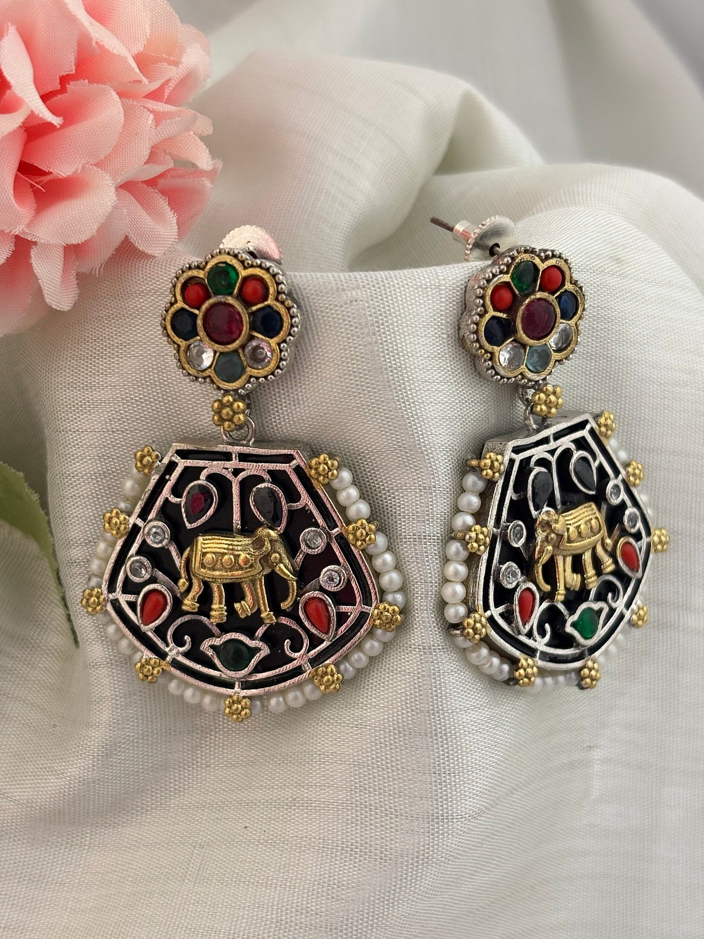 A pair of silver look alike earrings with multicolored stones and pearl fringes, featuring a golden elephant motif.