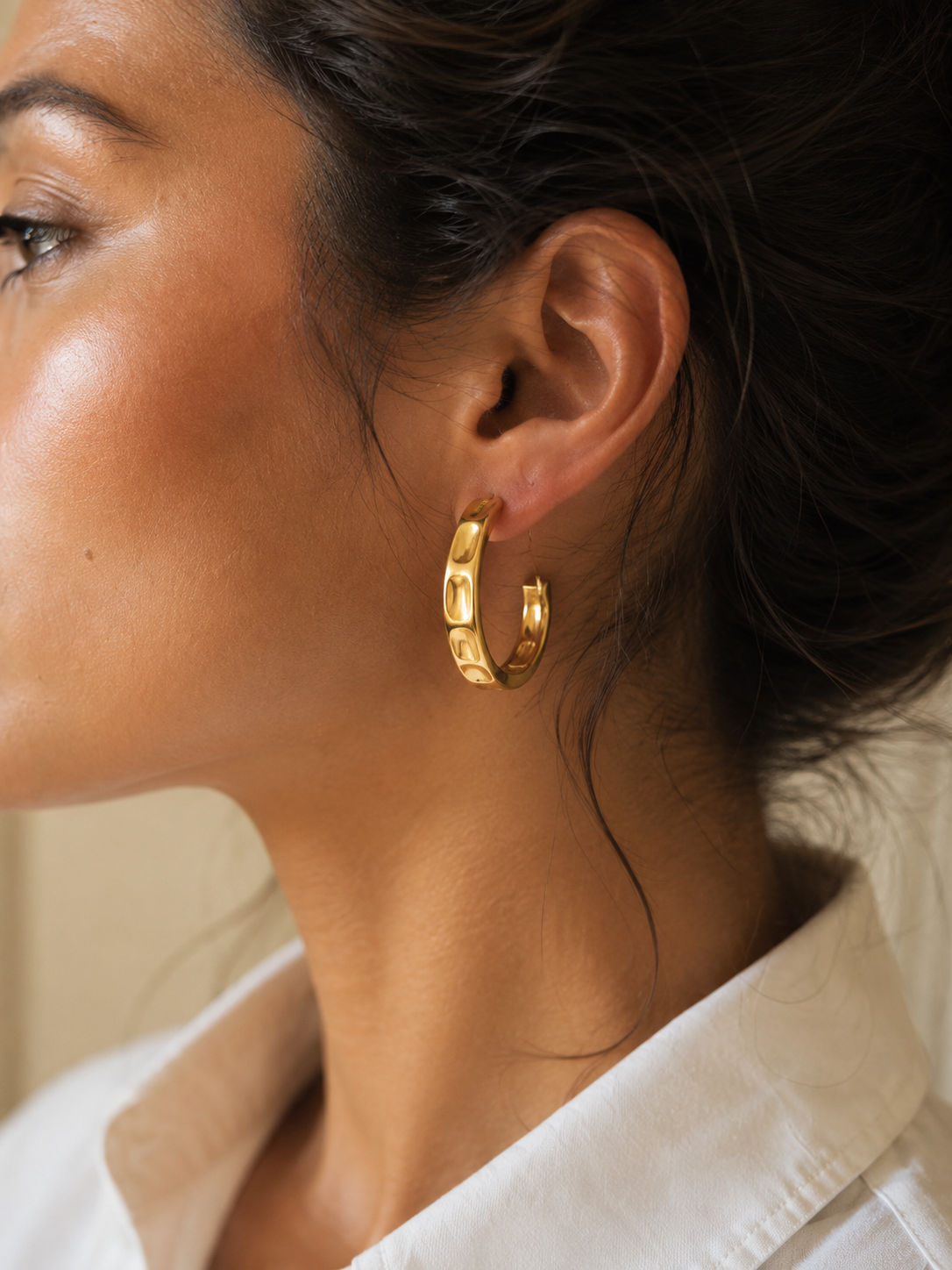 Close-up of a person wearing gold hoop earrings with a neutral background